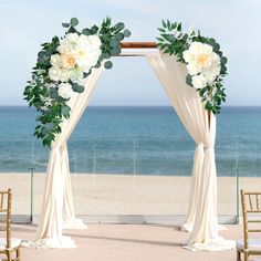 an outdoor wedding ceremony setup with white flowers and greenery on the arch over looking the ocean