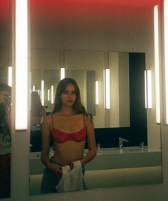 a woman standing in front of a bathroom mirror wearing a red bra and blue jeans