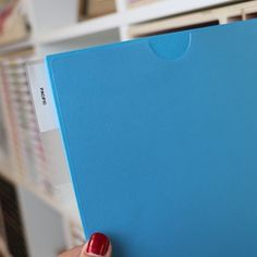 a person holding up a blue folder in their left hand with a red nail polish on it