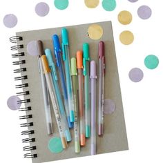 several pens are lined up on a notebook with confetti scattered around the pages