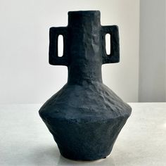 a large black vase sitting on top of a table next to a white wall and floor