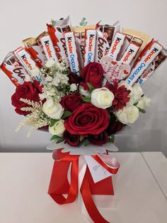 a bouquet of flowers and chocolates in a vase with a red ribbon around it