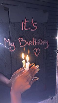 a woman holding two candles in front of a sign that says it's my birthday