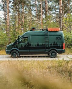 a green van parked on the side of a road in front of some tall trees