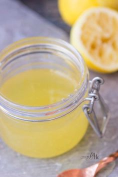 a glass jar filled with yellow liquid next to sliced lemons on a gray surface