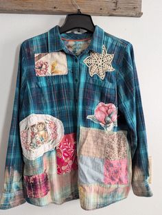 a blue shirt with patchwork on it hanging from a wooden hanger next to a white wall