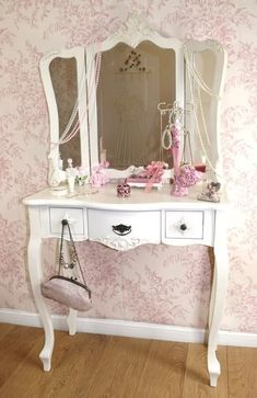 a white dressing table with mirror and purse on it in front of pink wallpaper