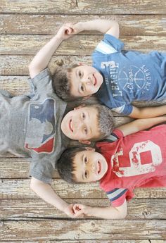 three young boys standing next to each other on top of a wooden floor with their hands in the air