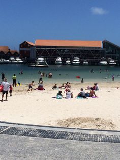 many people are on the beach and in the water at this point there is a boat dock