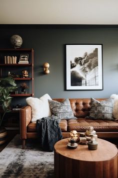 a brown leather couch sitting in a living room next to a wooden table and bookshelf