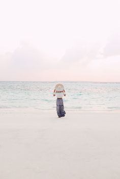 a woman standing on top of a sandy beach next to the ocean holding an umbrella