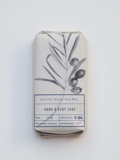 a bar of hand and body soap sitting on top of a white surface with leaves