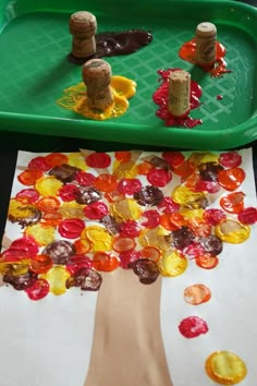 a child's hand is painting a tree with gummy bears on the paper