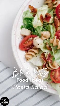 pasta salad with tomatoes and lettuce in a white bowl on a striped table cloth