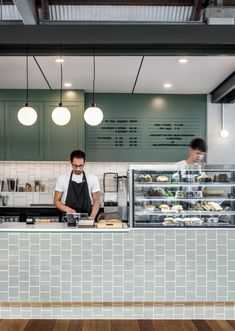 two men working behind the counter in a restaurant or cafe with wood floors and green walls