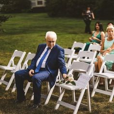 an older man sitting in a row of white folding chairs with flowers on each chair