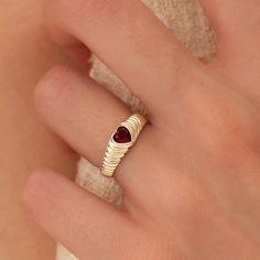 a woman's hand wearing a gold ring with a red stone in the middle