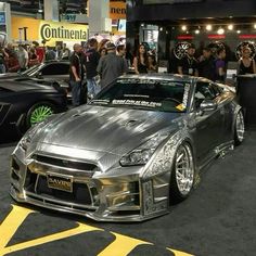 a silver sports car parked on top of a parking lot next to other cars and people