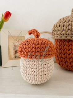 two crocheted pumpkins sitting on top of a white shelf next to a vase