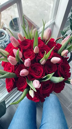 a woman holding a bouquet of red and pink tulips in her lap,