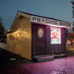 a psychic shop lit up at night on the side of a road with trees in the background