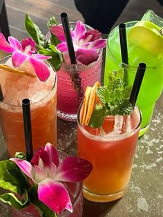 three different types of cocktails on a table with flowers in the middle and one has a lime