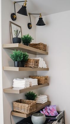 some shelves with towels and plants on them in the corner of a room that has white walls