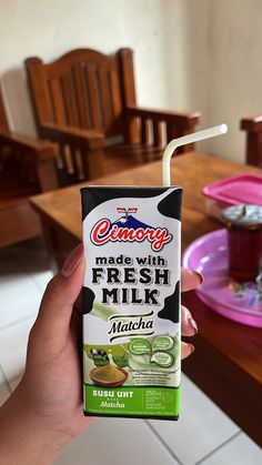 a person holding up a carton of fresh milk in front of a wooden table