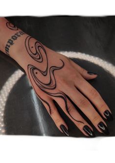 a woman's hand with black nail polish and tattoos on her left arm, sitting on a table