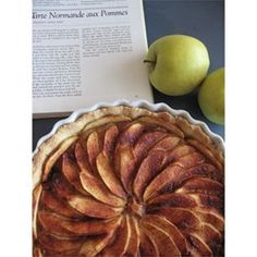 an apple pie sitting on top of a table next to two apples and a book