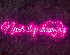 a neon sign that says never stop dreaming in the shape of a heart on a furry surface