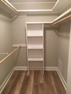 an empty walk - in closet with white shelving and wooden flooring is shown