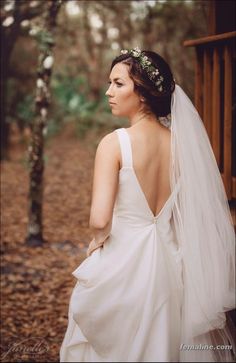 a woman wearing a wedding dress and veil standing in front of a wooden porch with leaves on the ground