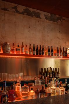 many bottles and glasses are lined up on the shelf in front of an empty bar