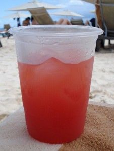 a plastic cup filled with liquid sitting on top of a sandy beach next to the ocean