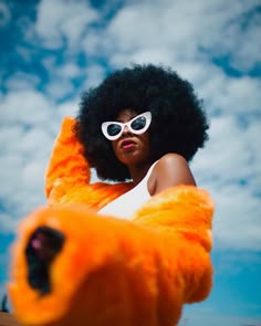 a woman wearing sunglasses and an orange fur coat is posing for the camera with her arms behind her back