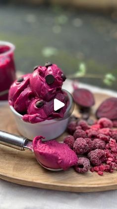 a wooden plate topped with red food next to a bowl filled with raspberries