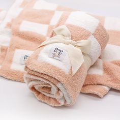 a pink and white checkered blanket with a bow on it's end is folded up