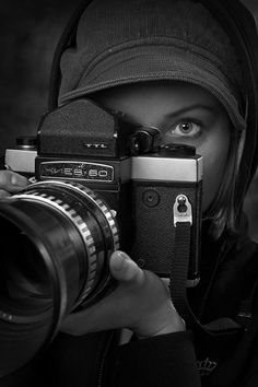 black and white photograph of a person holding a camera in front of their face with the hood on