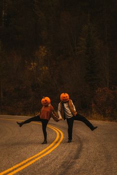 two people wearing pumpkin hats and holding hands on a road with trees in the background