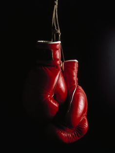 two red boxing gloves hanging from a rope on a black background with light coming through the window