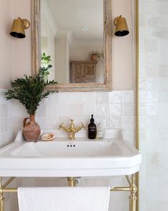 a white sink sitting under a mirror next to a gold faucet in a bathroom