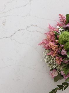 a bouquet of flowers sitting on top of a white marble countertop next to green leaves