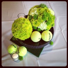 an arrangement of green flowers and tennis balls on a white table cloth with candles in the middle