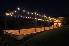 an outdoor area with lights and poles on the side of it at night, in front of a building