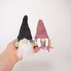 two crocheted gnomes sitting on top of each other's fingers in front of a white background