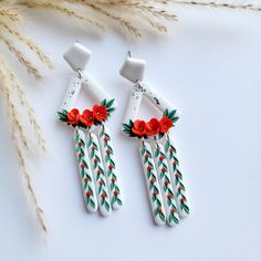 the earrings are decorated with red flowers and green leaves, along with long white sticks