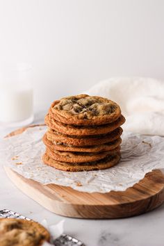 a stack of cookies sitting on top of a wooden cutting board next to a glass of milk