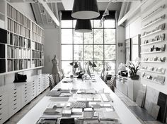 a long table with lots of books on it in front of large windows and shelves