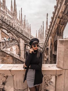 a woman standing on top of a stone wall next to a building with tall spires